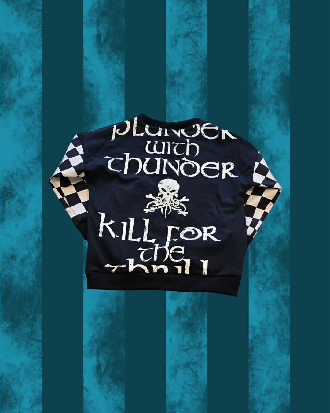 A black oversized Alestorm jumper with white gothic text reading 'plunder with thunder' and 'kill for the thrill', featuring a white skull and crossbones graphic on the front, white-and-black checkered sleeves, and a black ribbed hem and cuffs, displayed against a teal and dark blue vertically striped background.