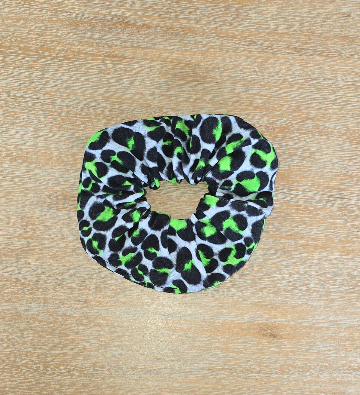 A green and black animal patterned scrunchie on a wooden surface.