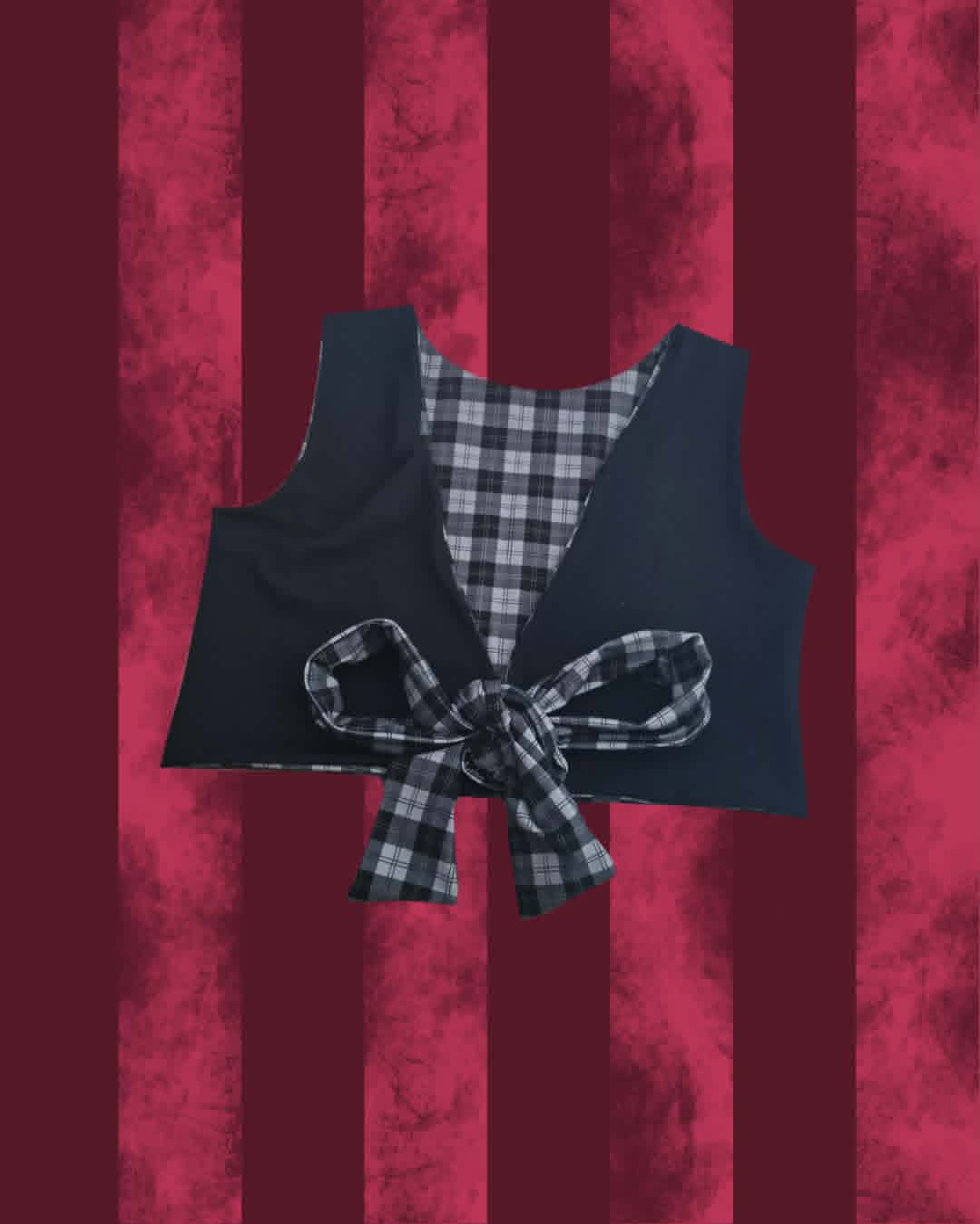 A cropped black vest with a black and gray plaid lining and a matching plaid bow tied at the front, displayed against a textured dark red and burgundy striped background.