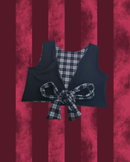 A cropped black vest with a black and gray plaid lining and a matching plaid bow tied at the front, displayed against a textured dark red and burgundy striped background.