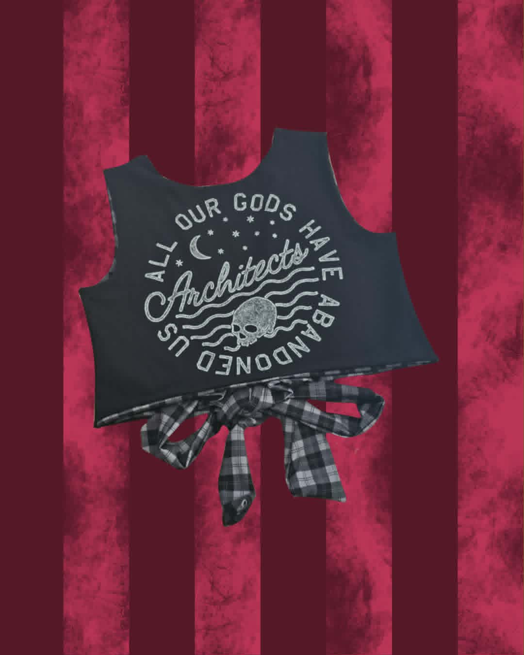 A sleeveless black top with a large white graphic reading 'All Our Gods Have Abandoned Us Architects' and a skull motif, tied at the waist with a plaid bow. The product is shown against a dark red vertically striped textured background.