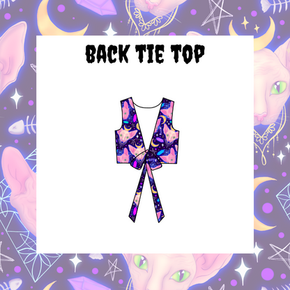 A back tie top featuring a multicolored tie-dye pattern on a purple background, displayed on a model with a fantasy-themed backdrop decorated with moons and stars.