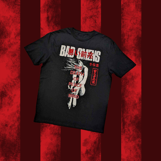 A black crew neck BAD OMENS t-shirt with a graphic print of text and a character, laid flat on a red striped background.