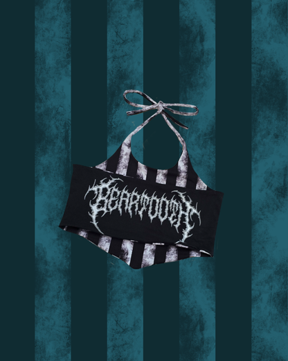 A black halter crop top with distressed white vertical stripes and a large white gothic-style 'BEARTOOTH ' logo across the chest, displayed against a dark teal striped background.