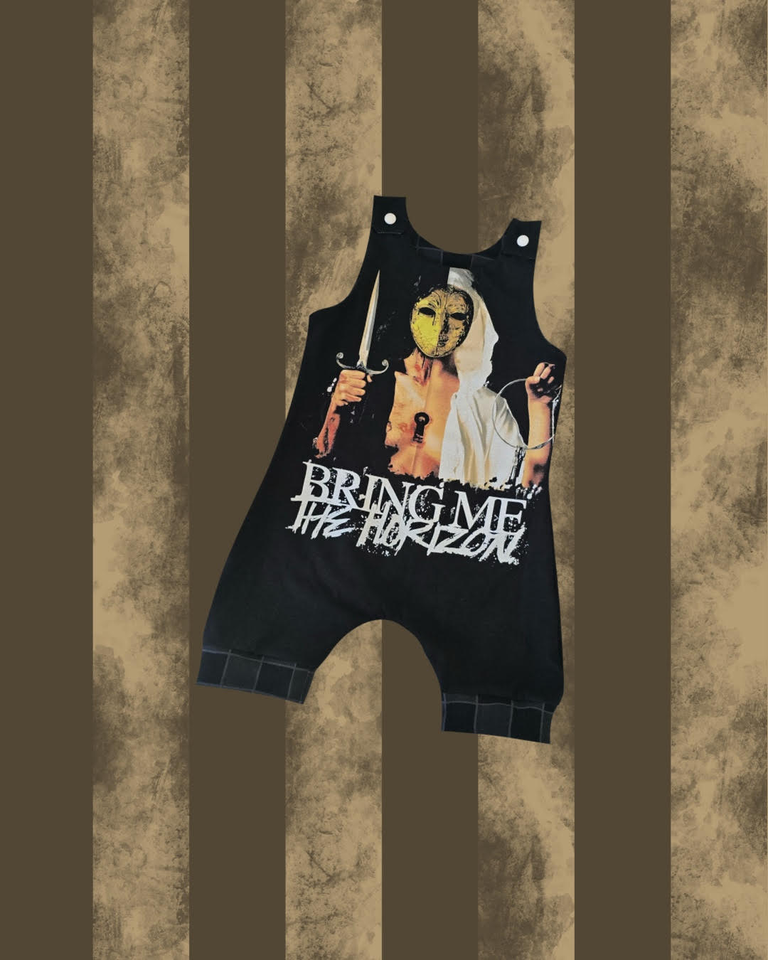 A black sleeveless romper or baby jumpsuit with a large graphic print of a masked figure holding a sword and the text 'BRING ME THE HORIZON', shown against a distressed brown and beige striped background.