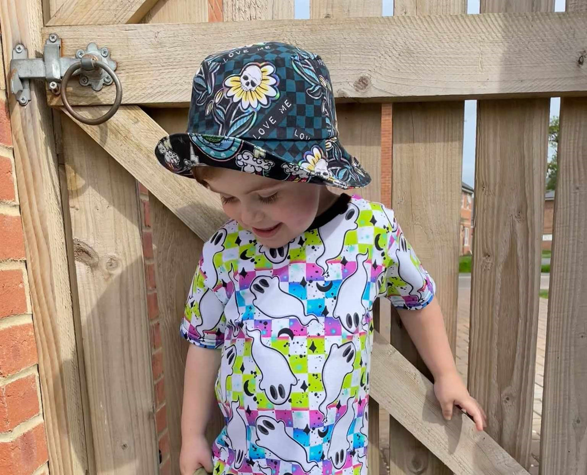 A child wearing a reversible bucket hat with one side featuring a floral pattern and the other side featuring a colorful animal pattern.