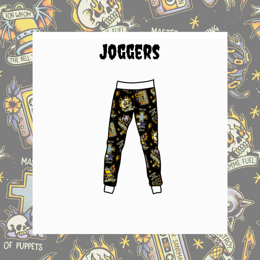 A pair of jogger pants with a black background and a colorful gothic tattoo-style print featuring skulls, crosses, and religious symbols, shown on a white card with the word 'JOGGERS' above it, set against a gray patterned background.