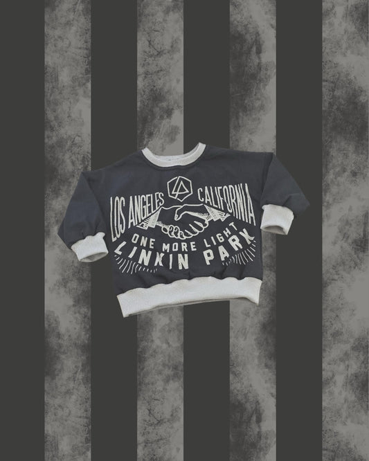 A dark gray crewneck sweatshirt with white ribbed trim and cuffs, featuring a white graphic print of Linkin Park logos and text, displayed against a dark gray and black vertically striped textured background.