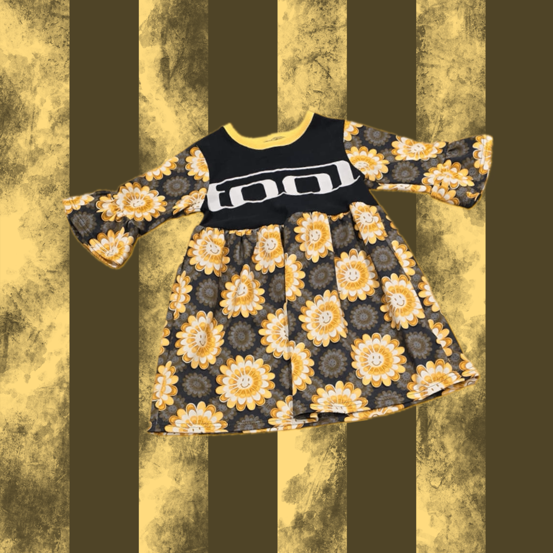A black SMOCK with a floral pattern and the text 'TOOL' on the front, displayed against a striped background.